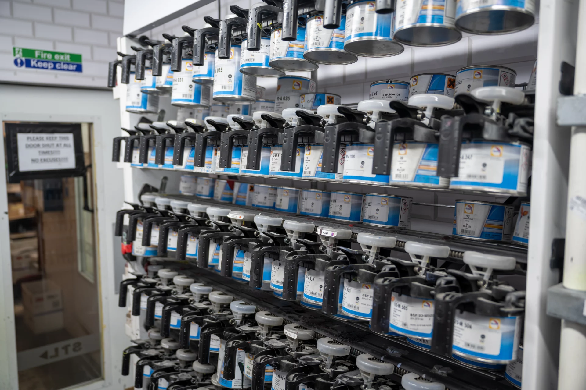 Rows of automotive paint toners and mixing cans on a colour-matching rack inside the Sandown Coachworks paint shop