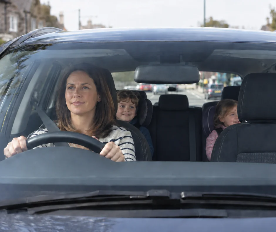 Woman driving a right-hand-drive family car with children seated behind her