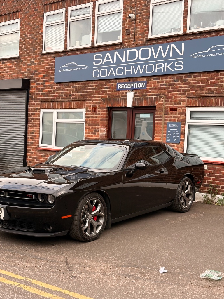 Prestige black Dodge Challenger parked outside Sandown Coachworks reception, showcasing pristine factory-level paint finish.