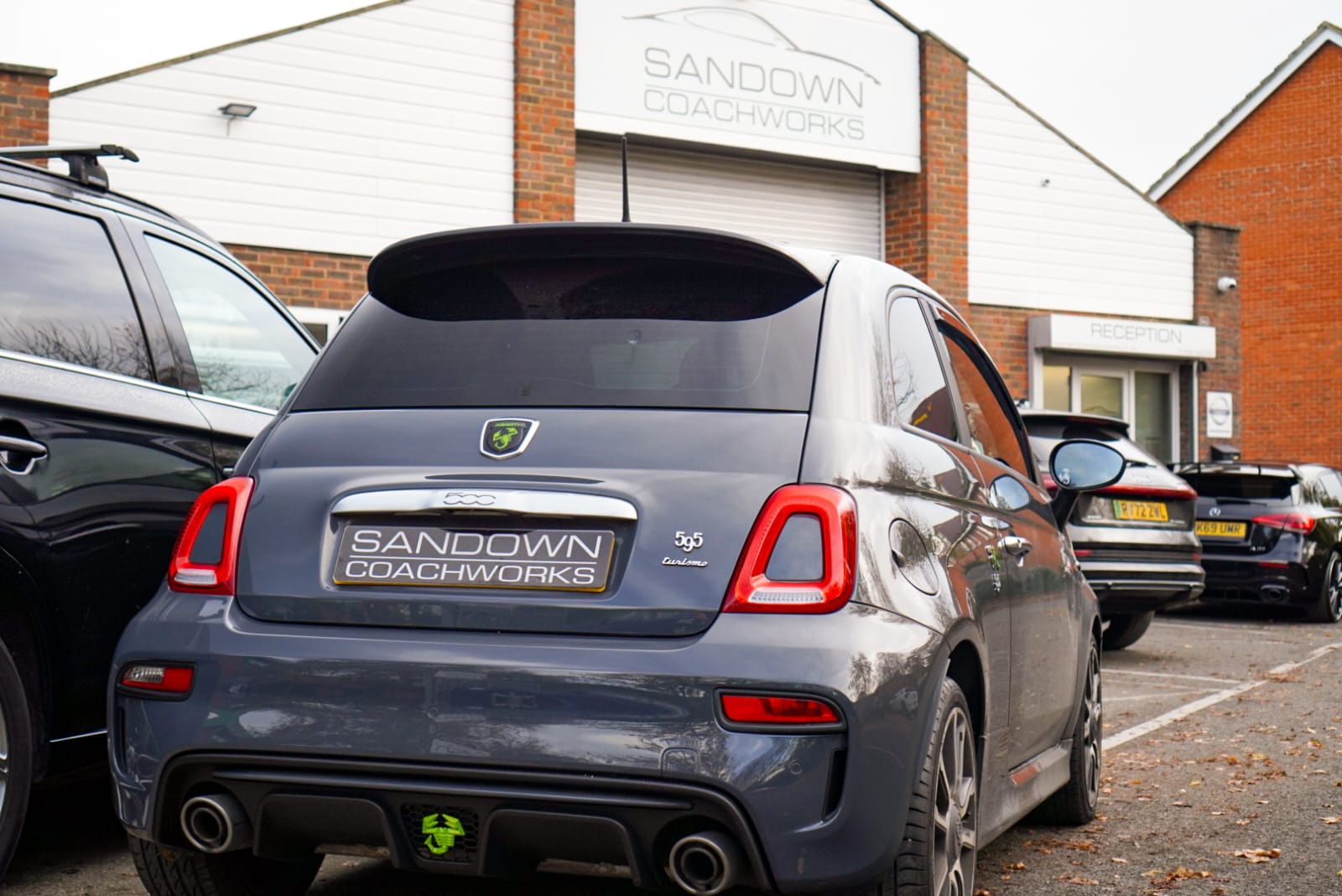 Grey Abarth 595 Competizione parked outside Sandown Coachworks with branded number plate, workshop signage visible above reception