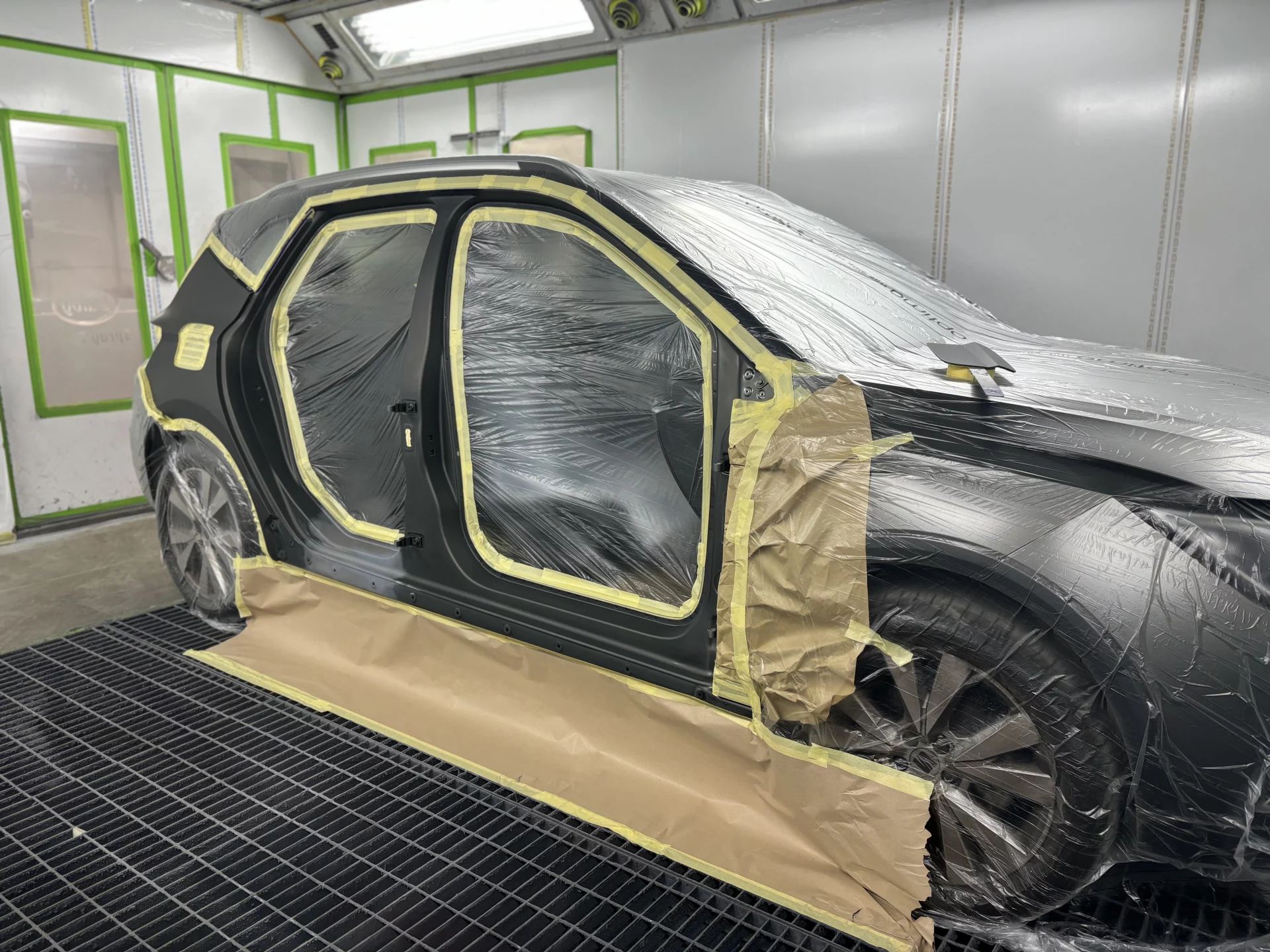 A vehicle professionally masked with protective film and tape inside a clean-room spray booth at Sandown Coachworks, prepared for high-quality paintwork.