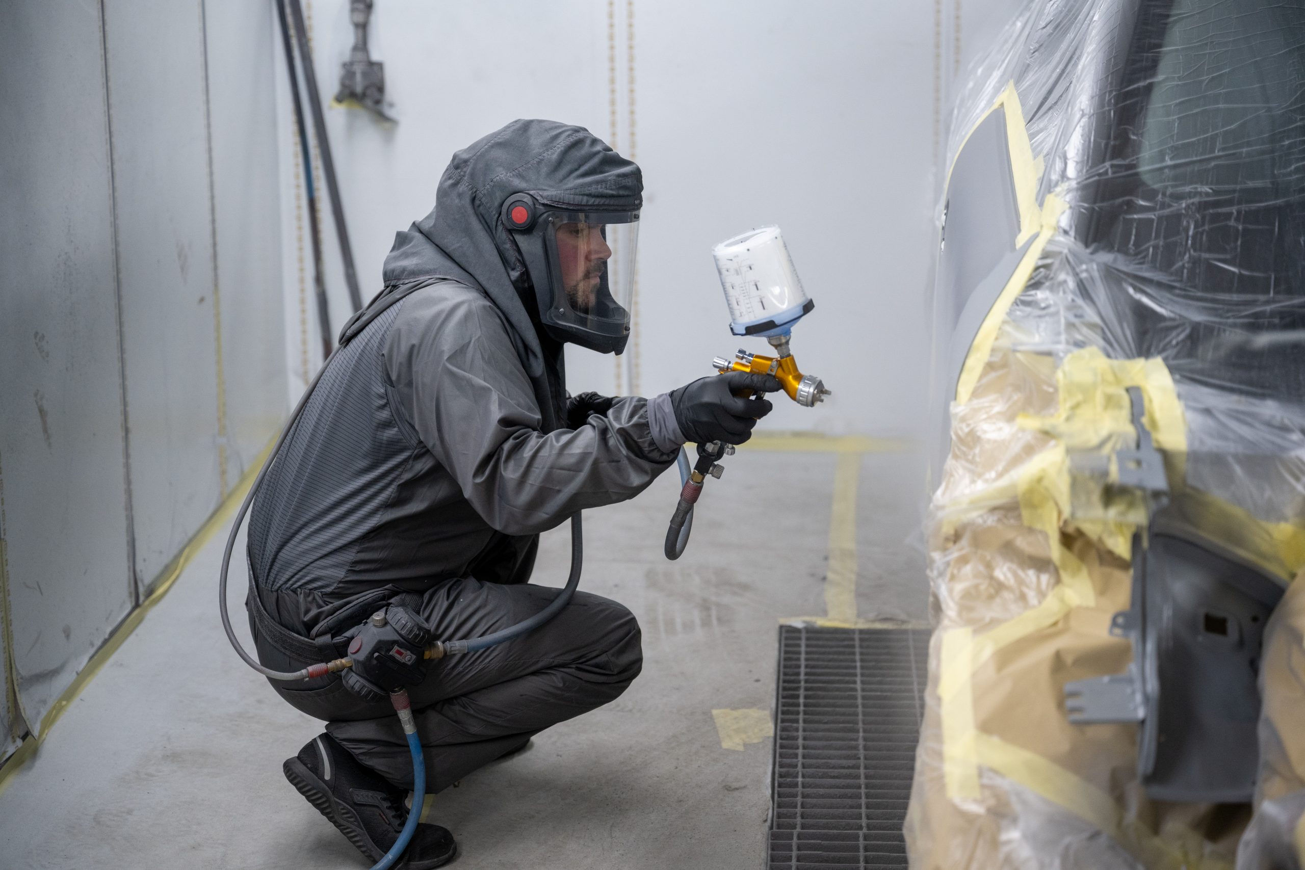 A technician in a full protective respirator suit using a professional spray gun in a controlled paint booth at Sandown Coachworks.