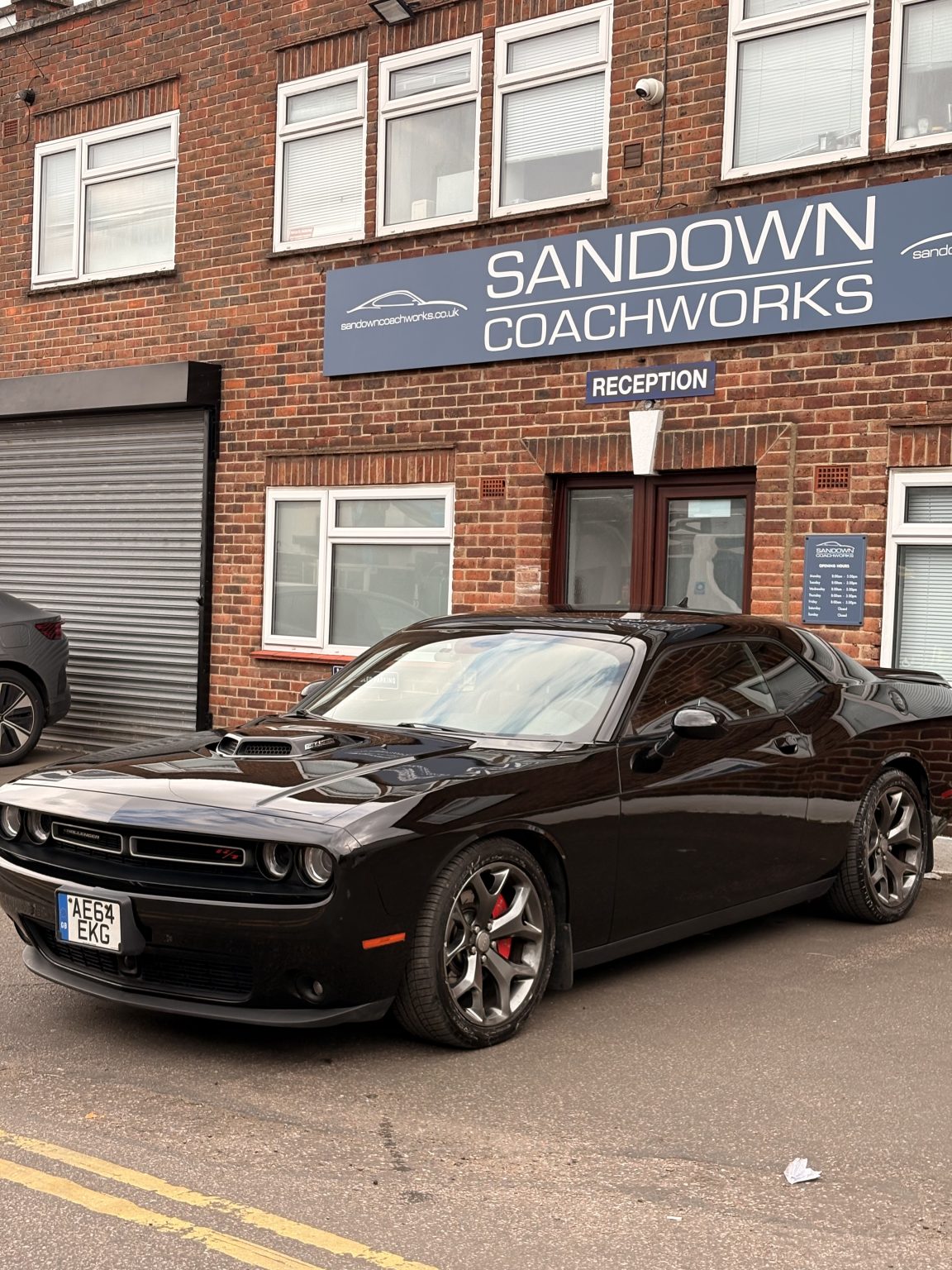 Prestige black Dodge Challenger parked outside Sandown Coachworks reception, showcasing pristine factory-level paint finish.