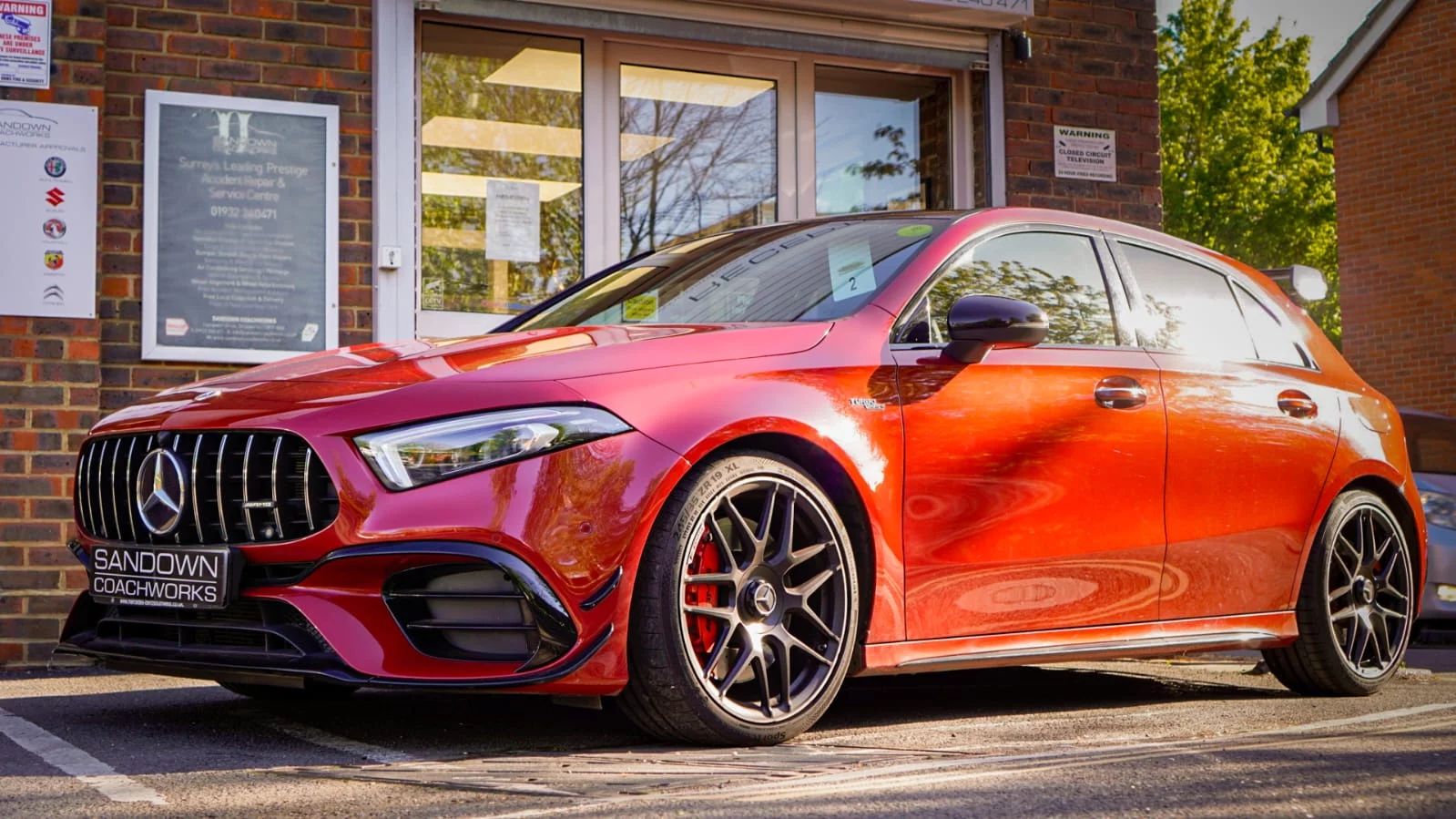 A high-performance red Mercedes-AMG A45 parked in front of the Sandown Coachworks accident repair and service centre in Shepperton.