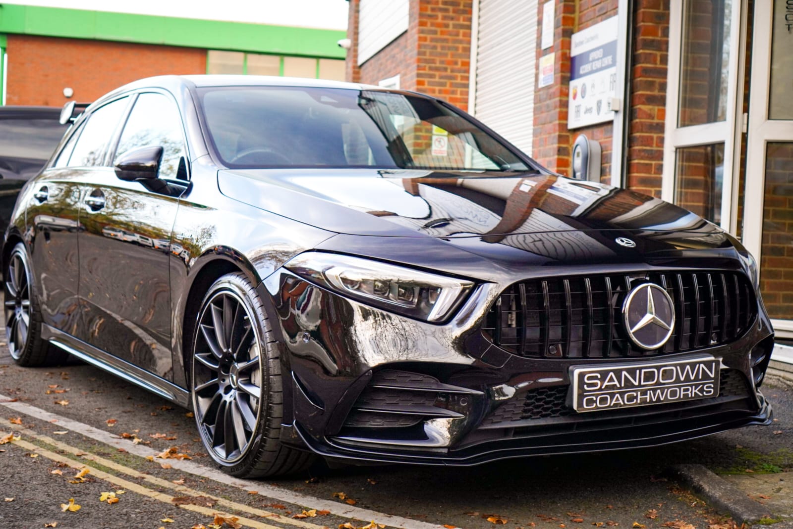Front-angle view of a deep metallic black Mercedes-AMG performance hatchback with a Sandown Coachworks number plate, showcasing perfect paint-matching reflections and an aggressive front grille.