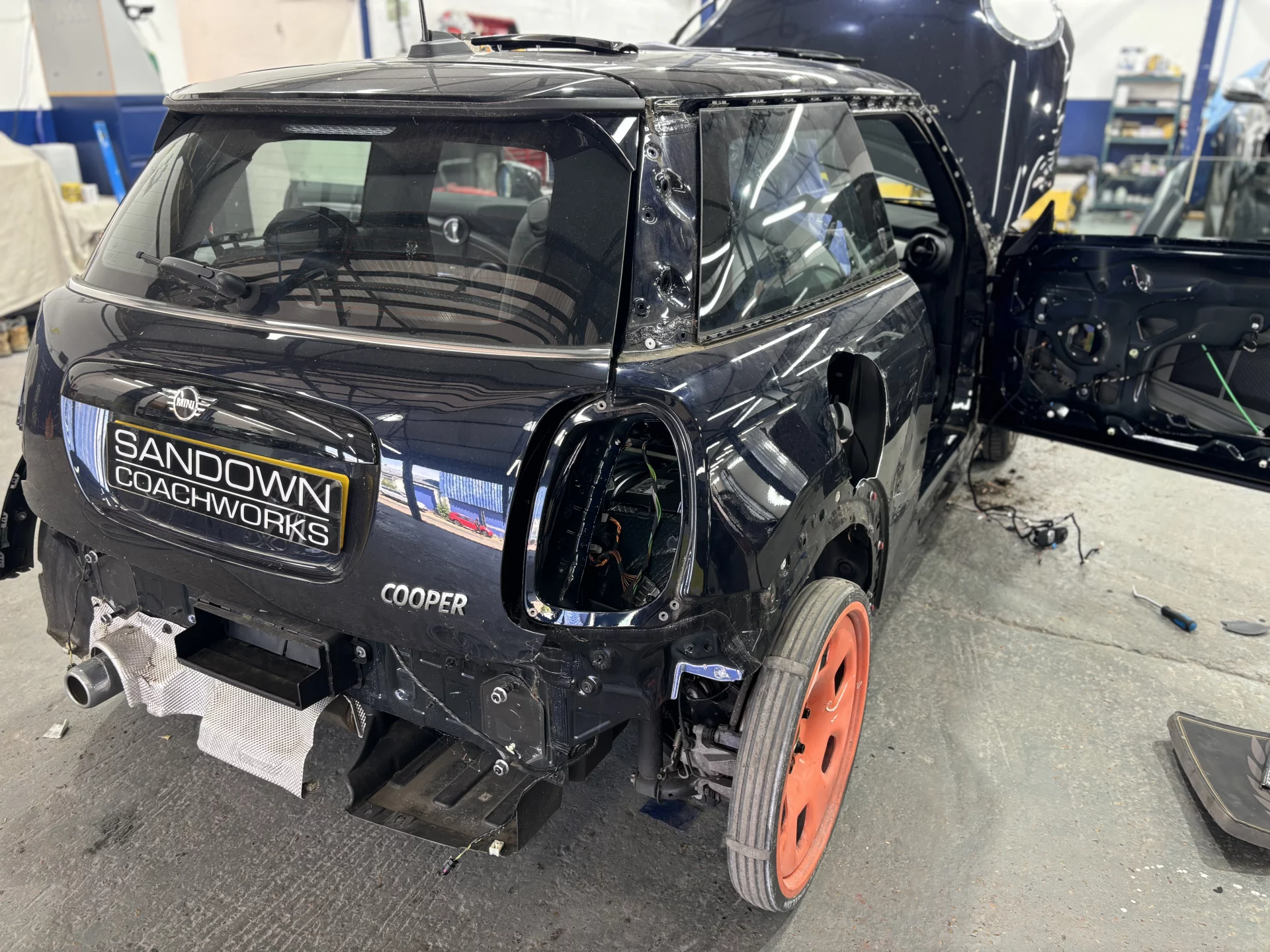 A black Mini Cooper being stripped down at Sandown Coachworks for a rear quarter panel repair, showing internal components and protective covers.