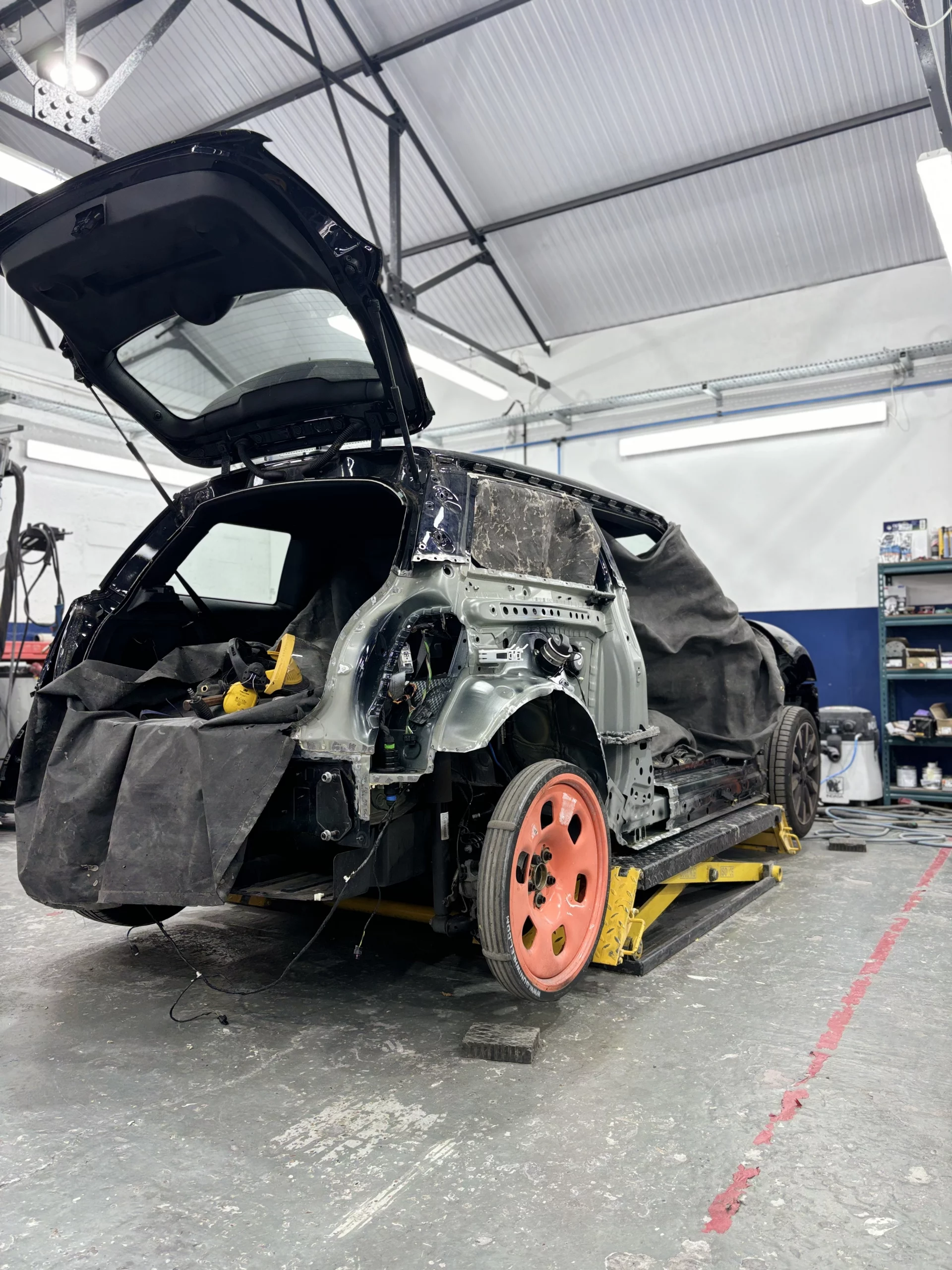 The structural repair stage at an approved bodyshop where the damaged rear panel of a Mini Cooper has been removed to inspect the chassis.
