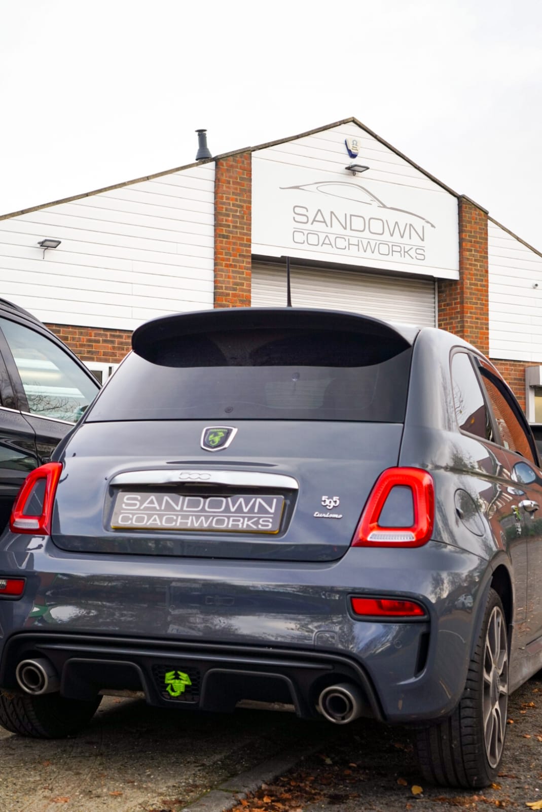 A grey performance hatchback parked in front of the Sandown Coachworks building, showcasing the official facility signage and manufacturer-approved repair environment.
