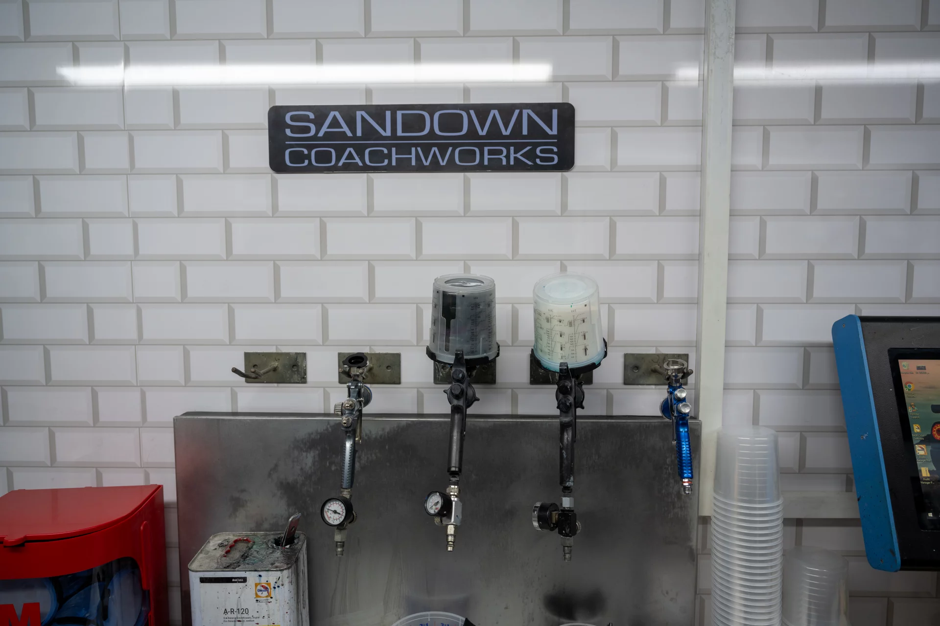Interior view of the Sandown Coachworks Shepperton facility showing the branded signage above a clean, organized paint preparation station with professional spray guns.